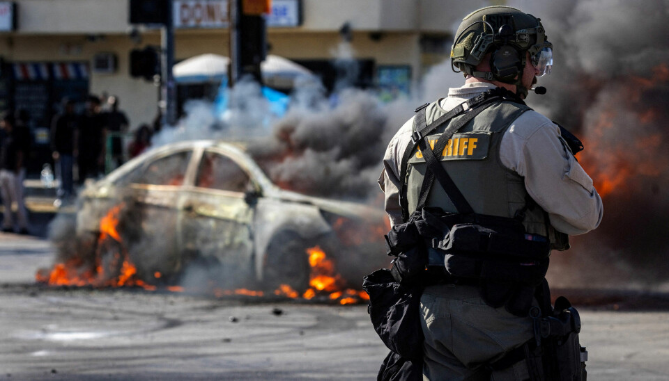 Røyk stiger opp fra en brennende bil under en konfrontasjon mellom demonstranter og politiet, etter flere pågripelser utført av immigrasjonsmyndighetene (ICE), i byen Compton i Los Angeles lørdag.